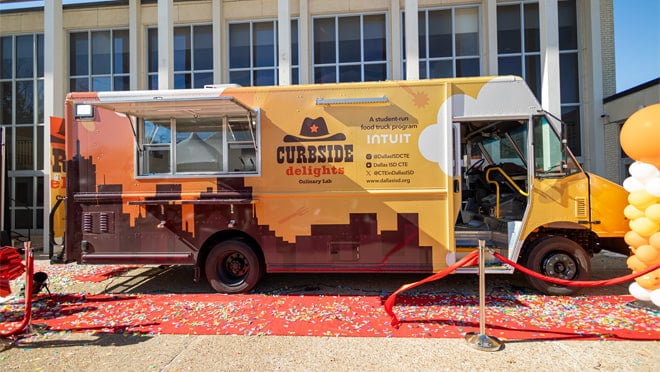 A food truck parked in a building with people standing outside of it.