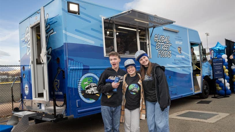 Three people standing in front of a blue truck.