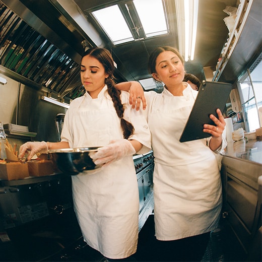 Two people in a kitchen holding up a camera.