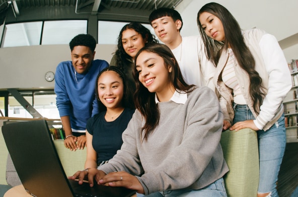 A group of students, looking at a laptop, smiling. 