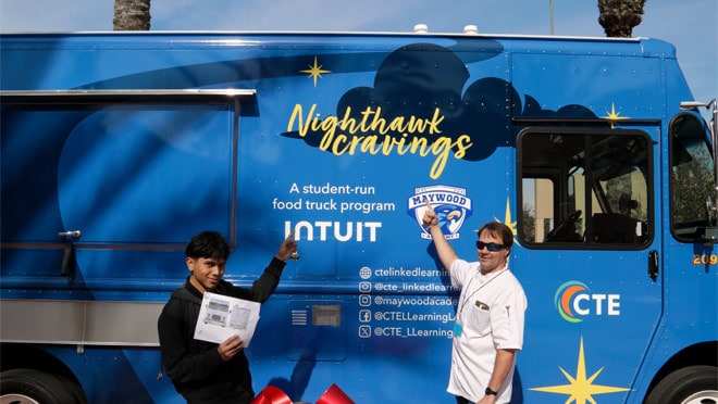 Two people standing in front of a food truck.