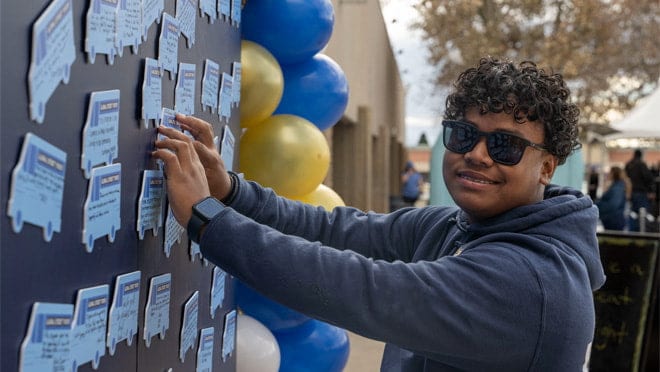 A person in a blue shirt is smiling next to a wall of framed cards.